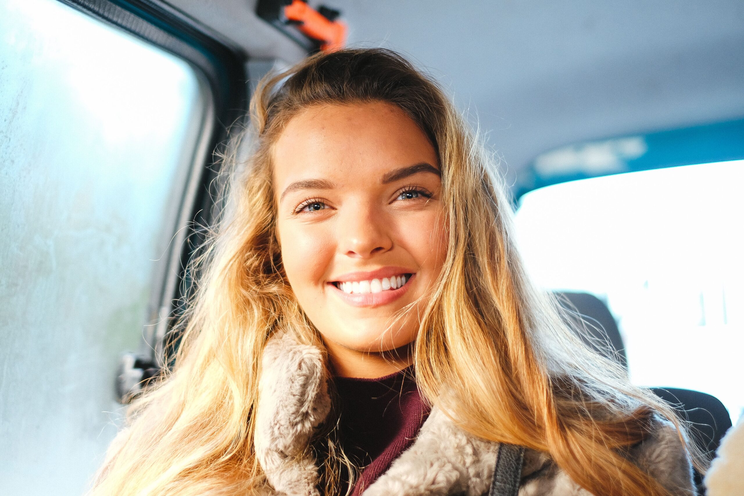 blonde woman smiling widely whilst sat in the back of a taxi